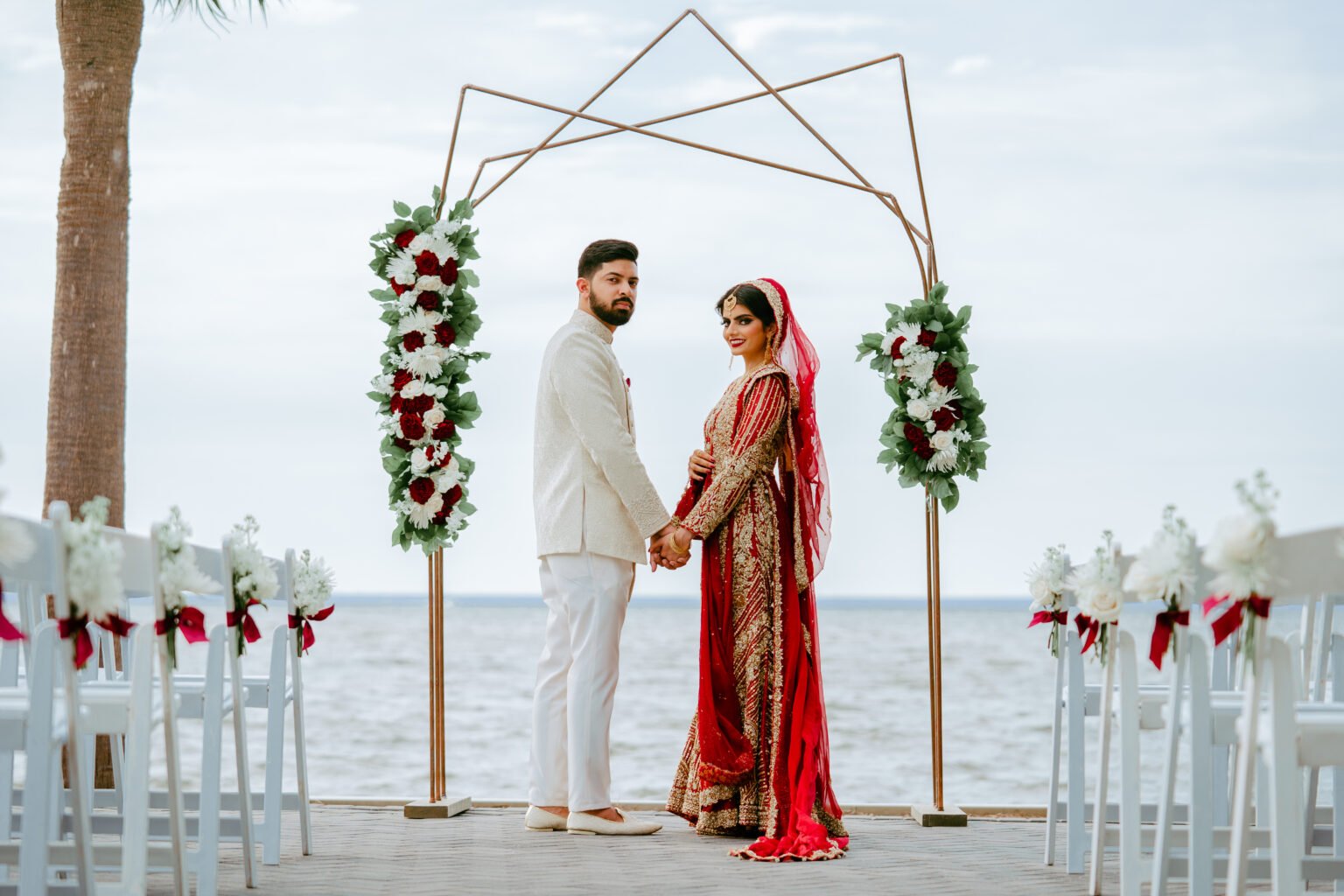 A couple beneath a floral wedding arch overlooking the water