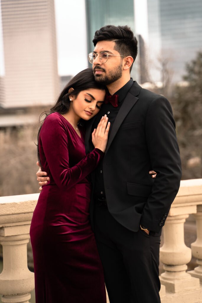 Woman in a burgundy dress resting her head against her partner on a city bridge.
